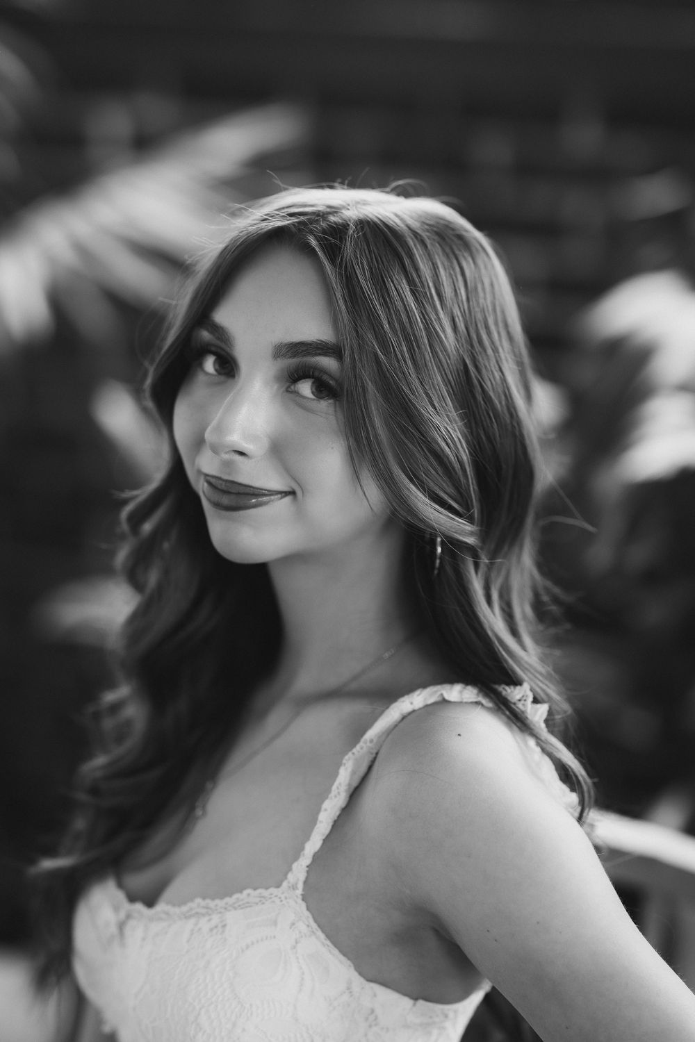 Black and white portrait of young woman with wavy hair in white lace dress smiling softly.
