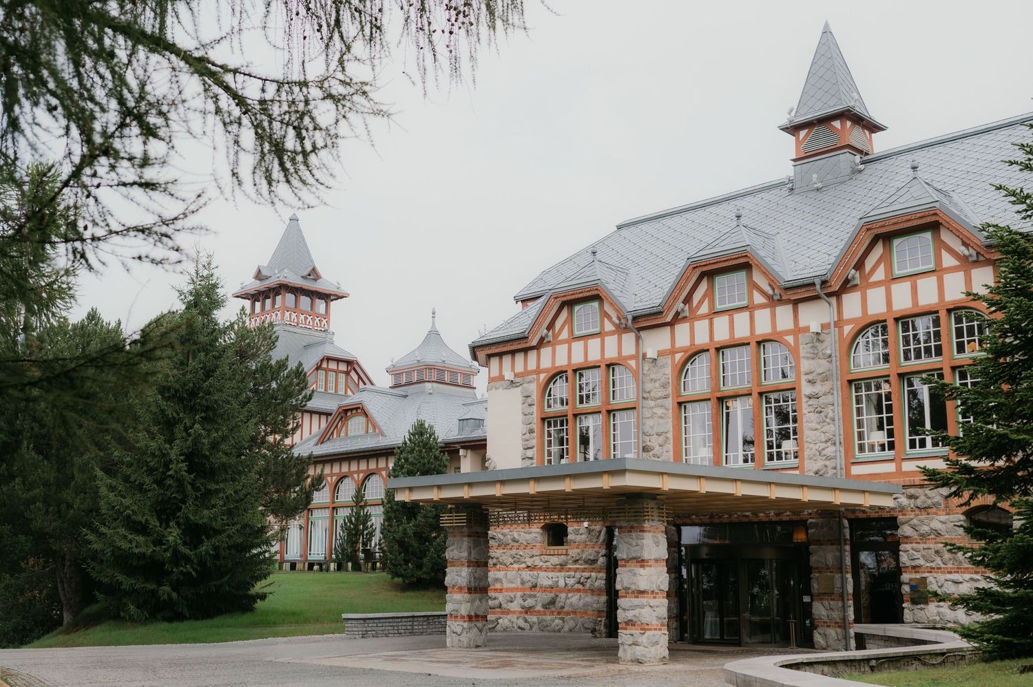 Historic castle-style hotel with stone facade, pointed turrets, and large windows surrounded by lush green trees.