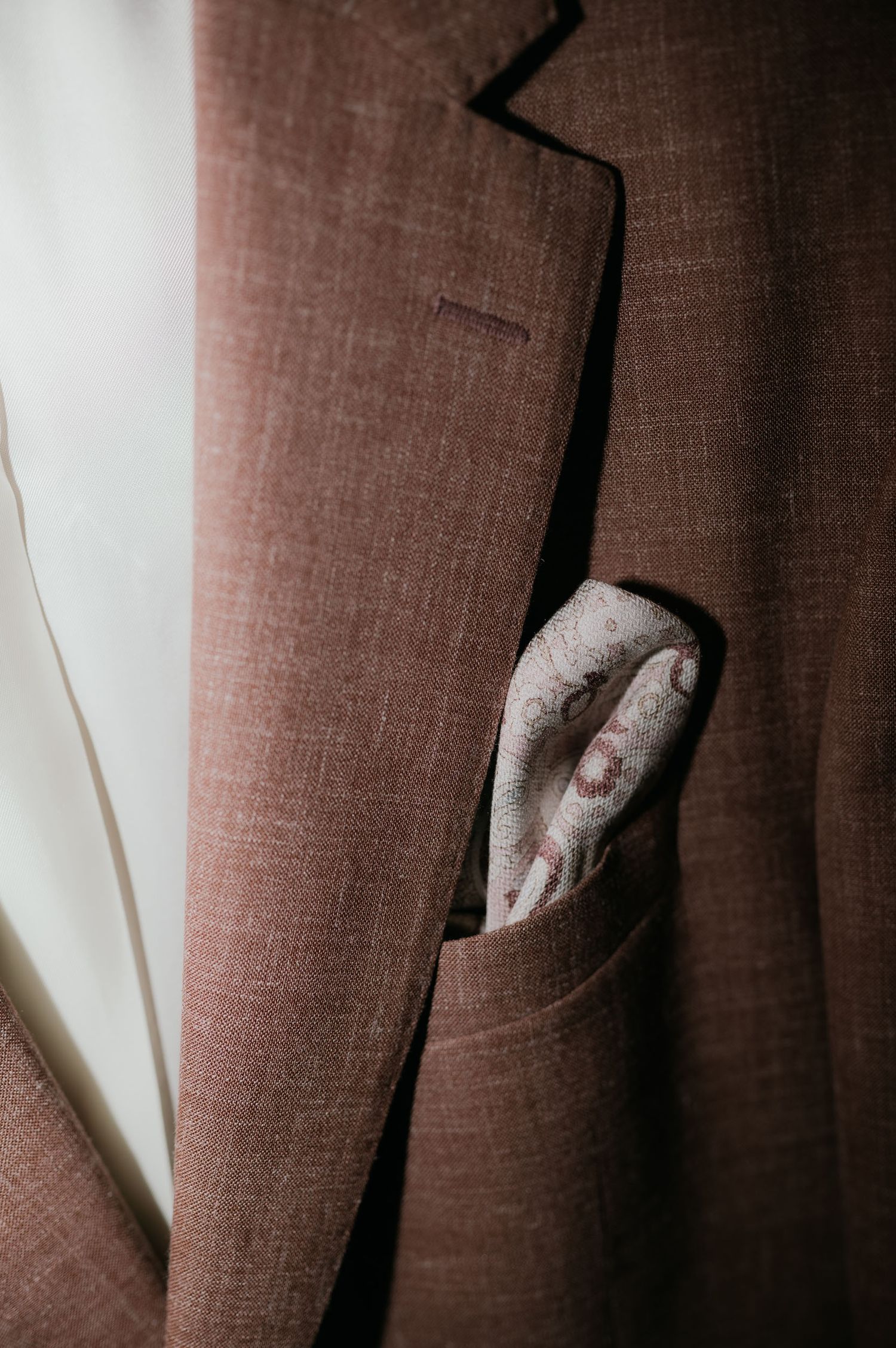 Close-up of a brown linen blazer with a floral pocket square neatly folded in the breast pocket.