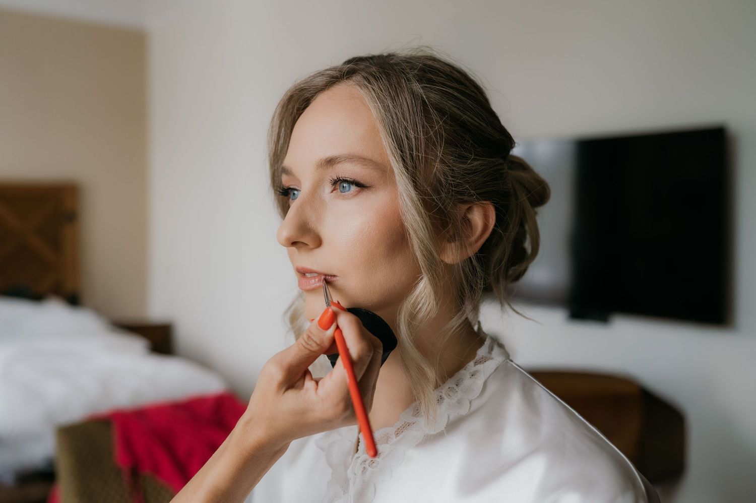 Bride getting makeup applied with a red brush while wearing a white robe, preparing for her wedding day.