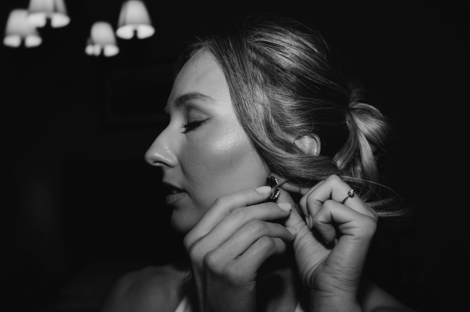 Black and white photo of a bride putting on earrings while getting ready for her wedding day.