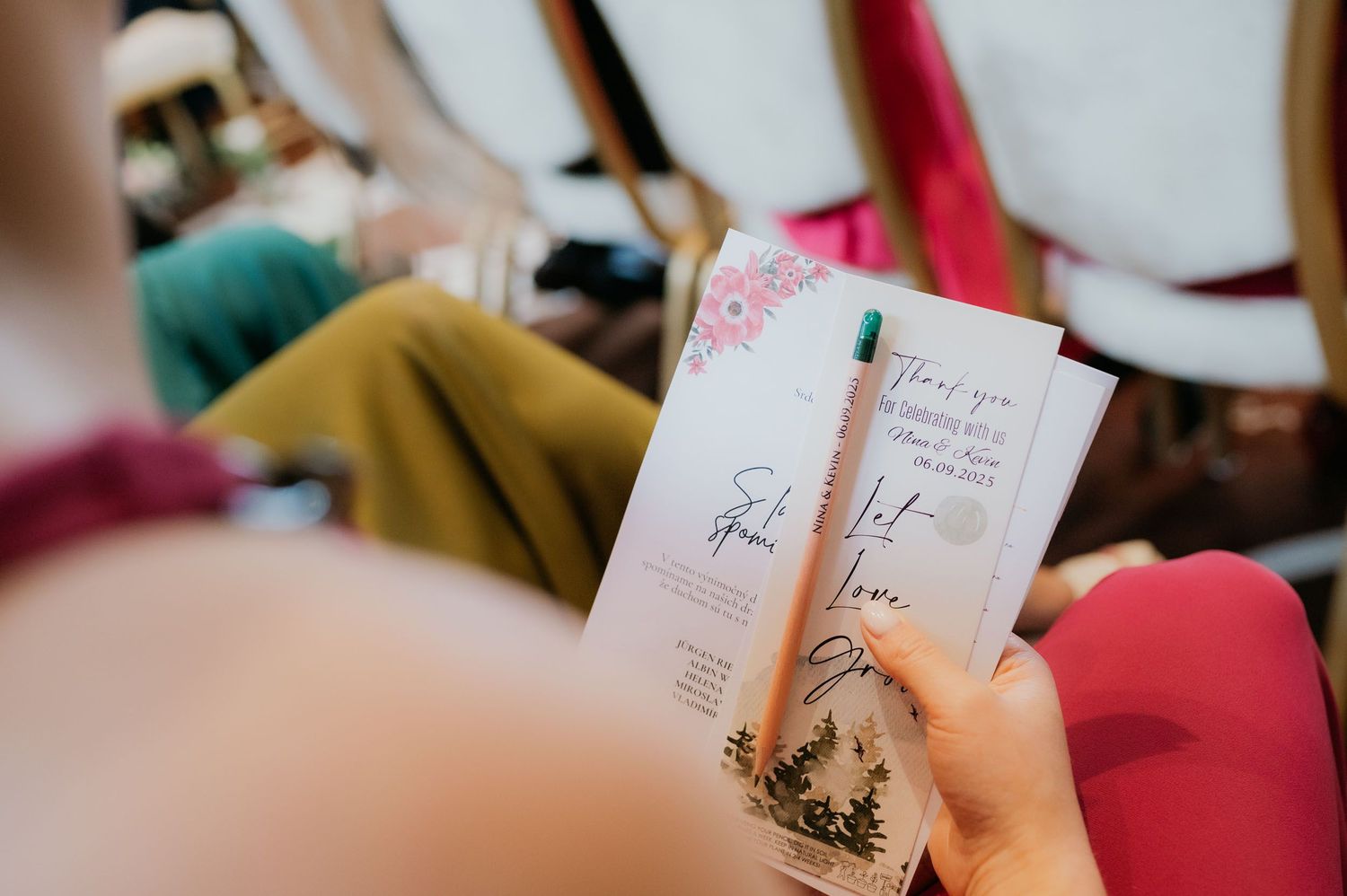 Person holding elegant wedding program cards with floral design at an outdoor ceremony.