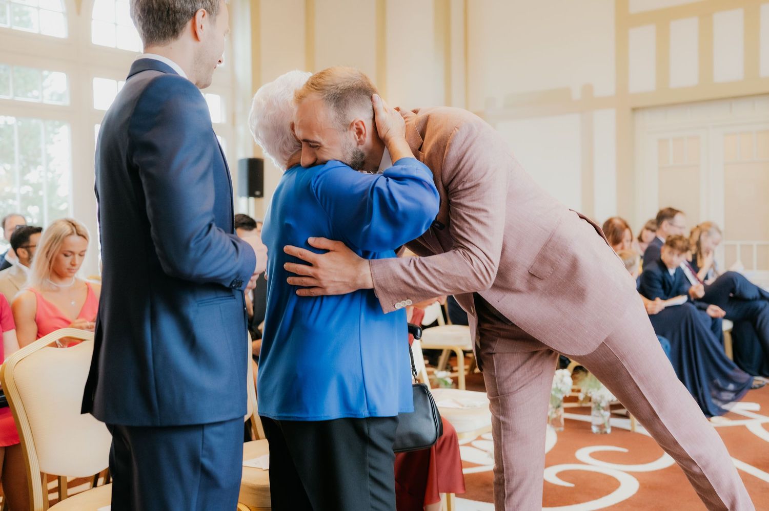 Guests sharing warm embraces and congratulations during an elegant wedding ceremony reception indoors.