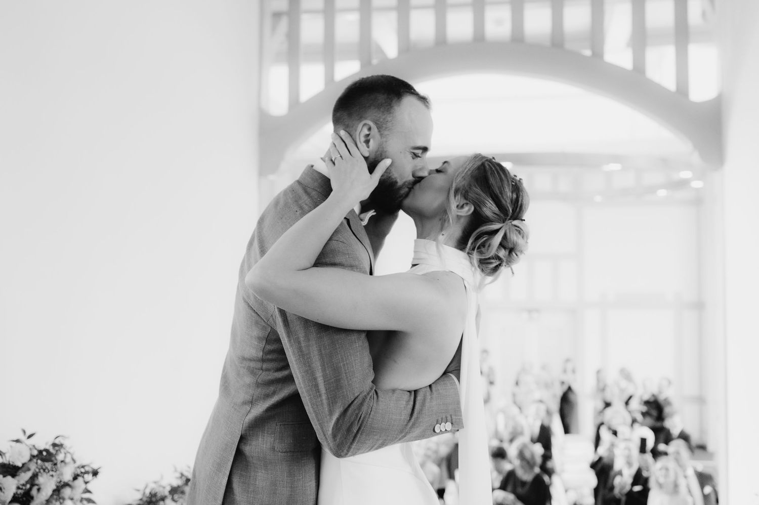 Black and white photo of a bride and groom sharing their first kiss at a wedding ceremony.
