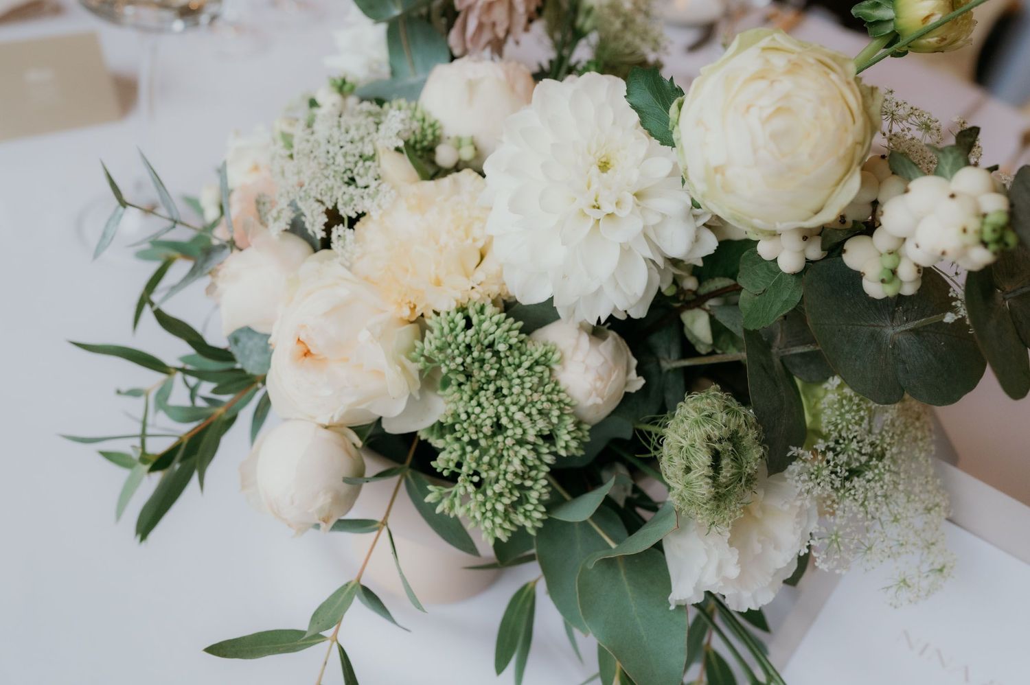 Elegant wedding centerpiece with white dahlias, ranunculus, blush peonies, green scabiosa, and eucalyptus foliage.