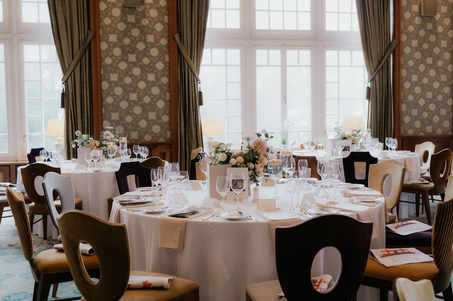 Elegant wedding reception room with round tables set with white linens, floral centerpieces, and glassware in a classic venue.