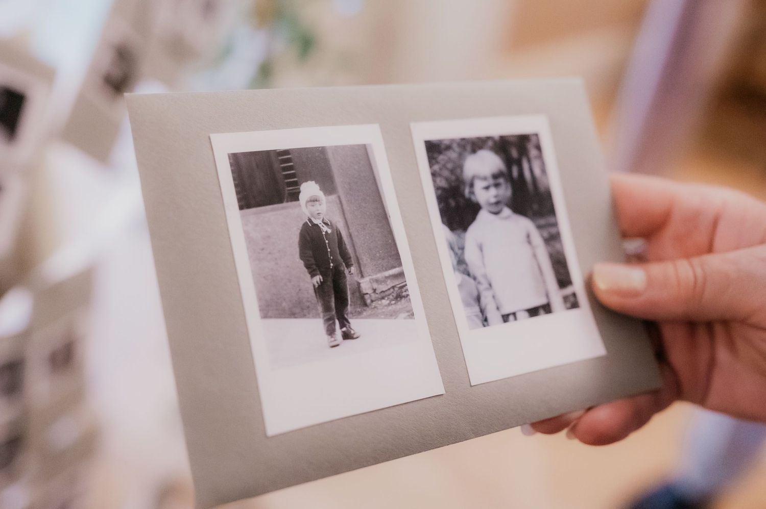 Hand holding a vintage photo album with two black and white Instax photos of young children in retro clothing.