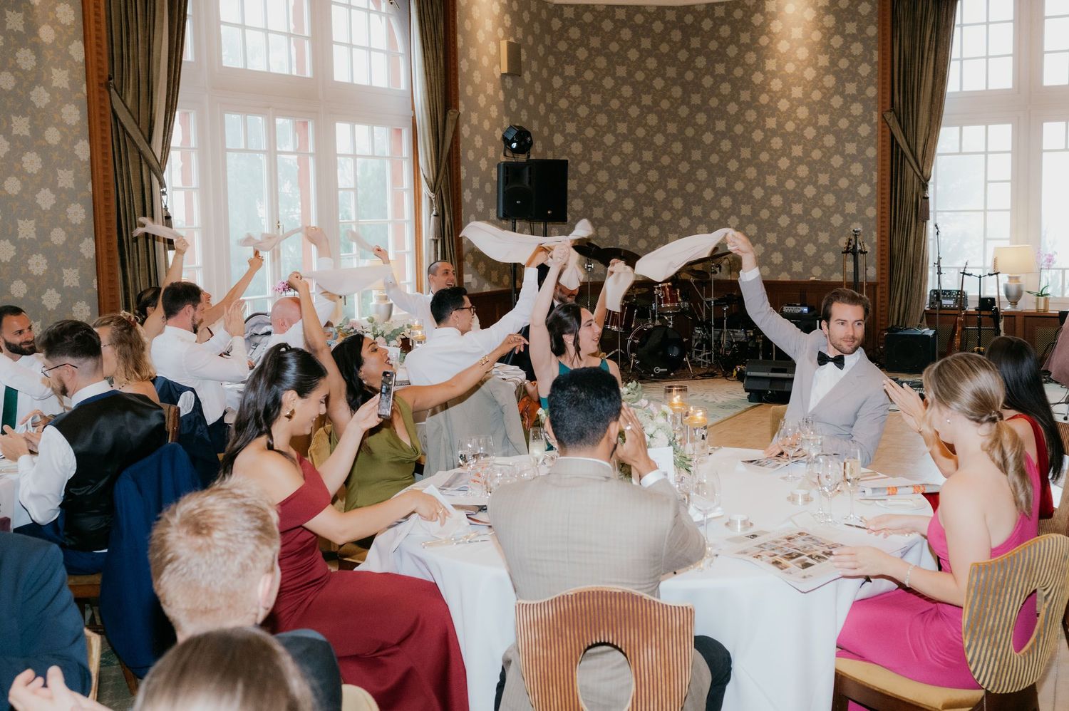 Wedding guests raise napkins in celebration at an elegant banquet hall reception dinner.