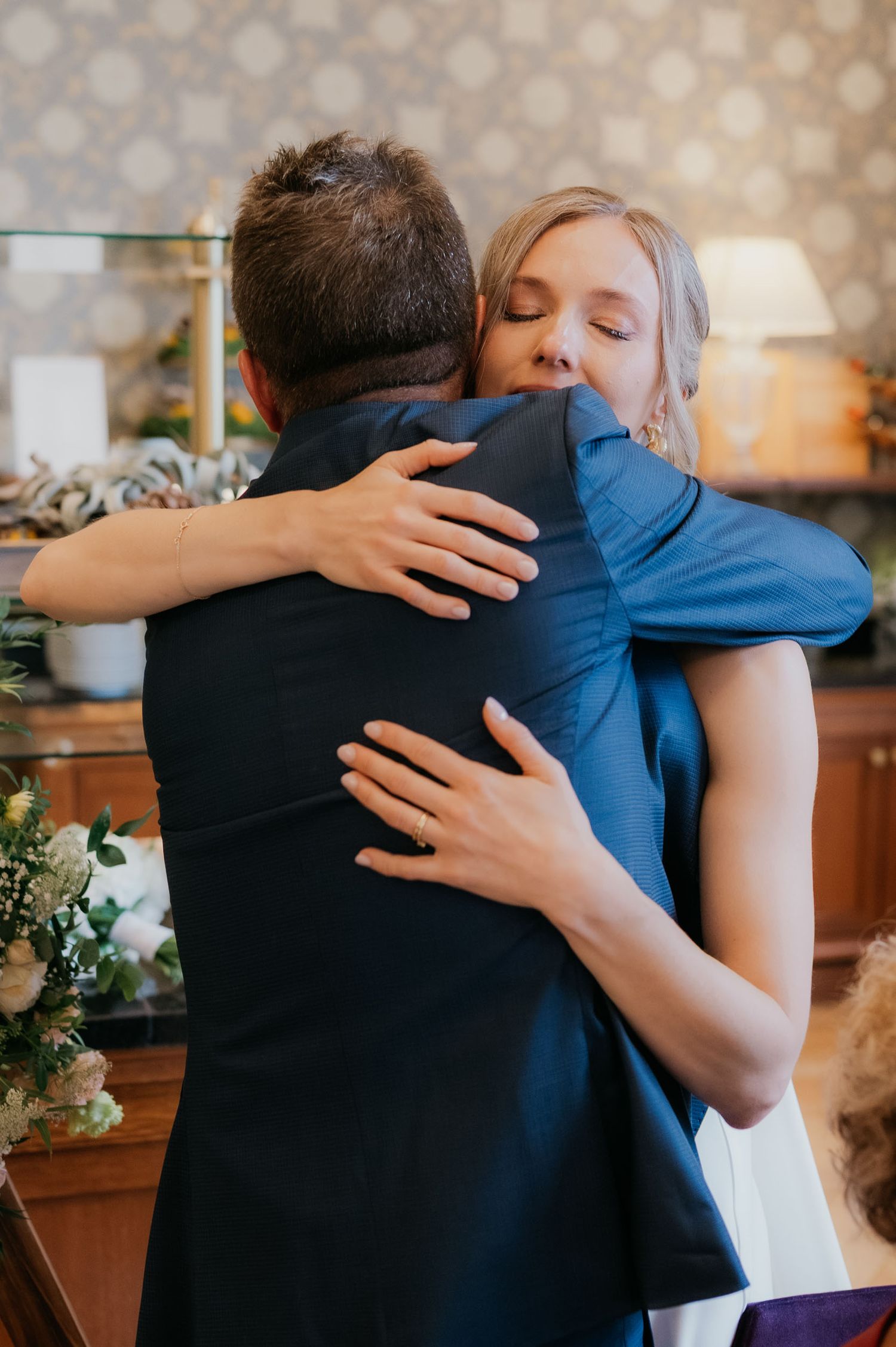 A bride and groom share an emotional hug during their wedding ceremony indoors.