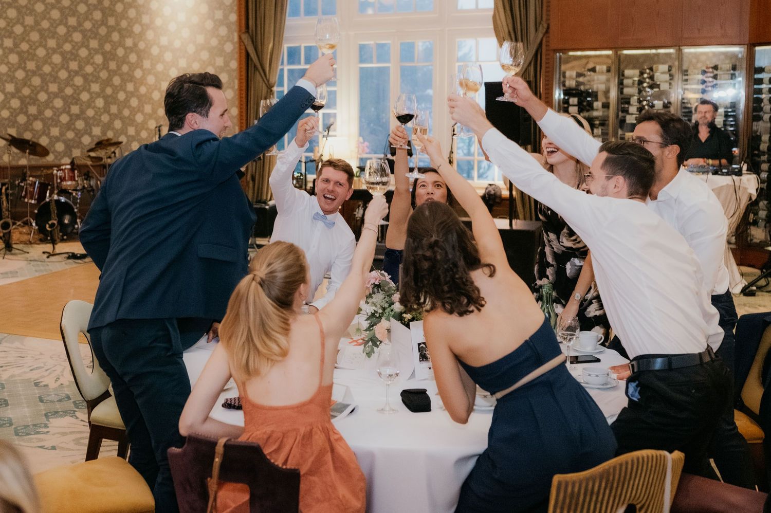 Wedding guests raising glasses in a joyful toast at an elegant reception dinner, celebrating with wine and champagne.