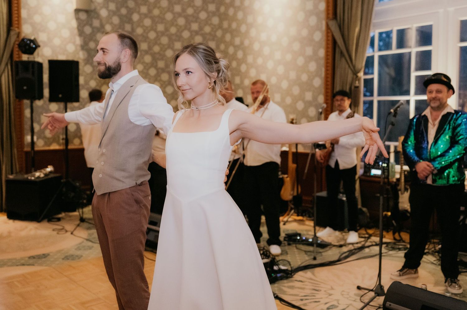 Bride and groom share first dance at wedding reception with live band performing on stage in elegant ballroom.