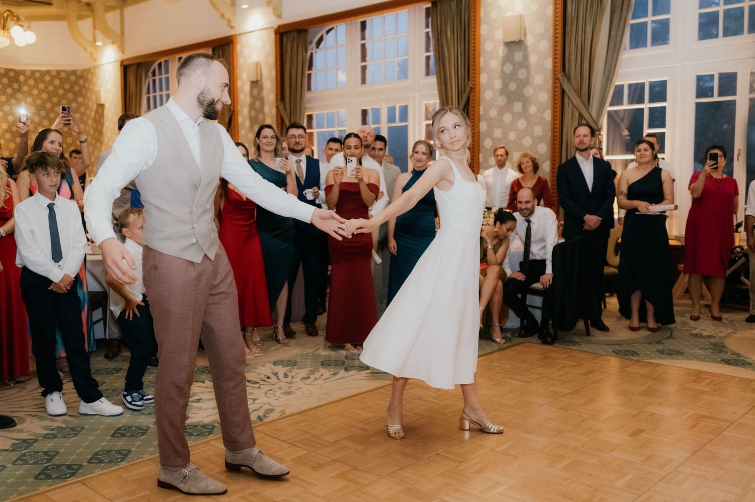 Bride and groom share their first dance at elegant wedding reception with guests watching in formal attire.