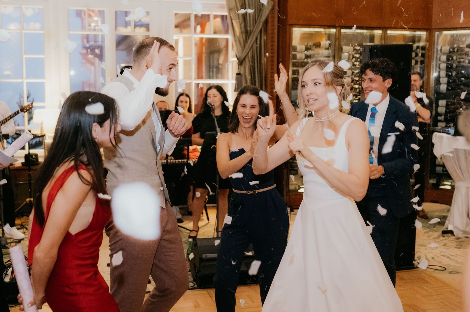 Bride and groom dancing joyfully with guests at wedding reception while confetti flies through the air.