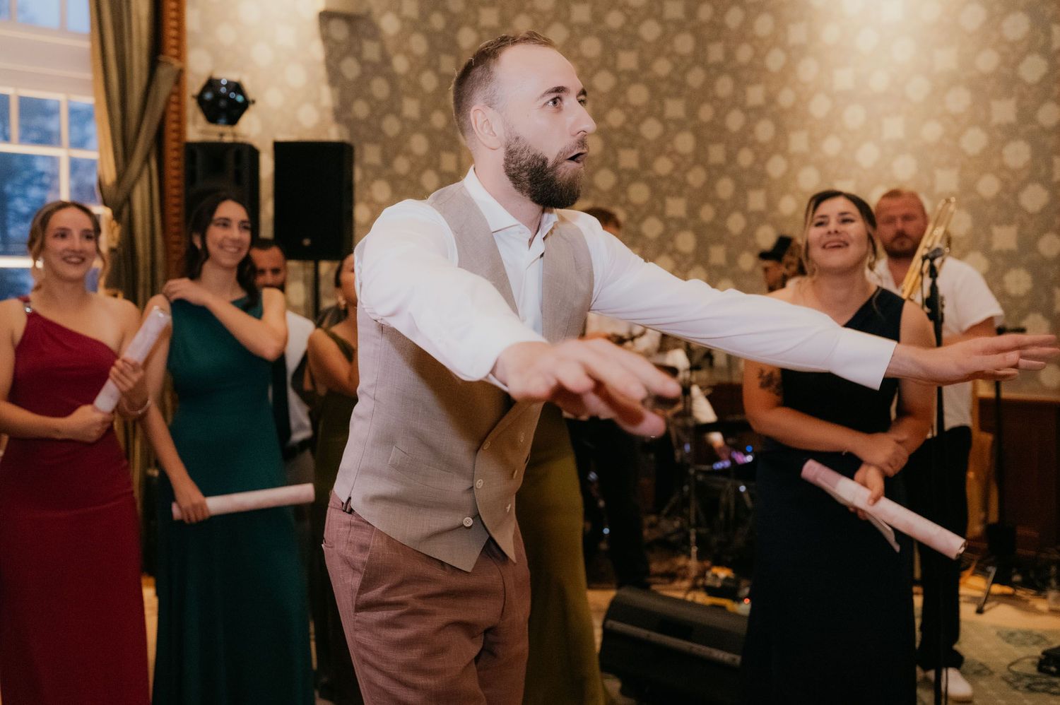 Groom dancing energetically with wedding guests in elegant ballroom during reception celebration.