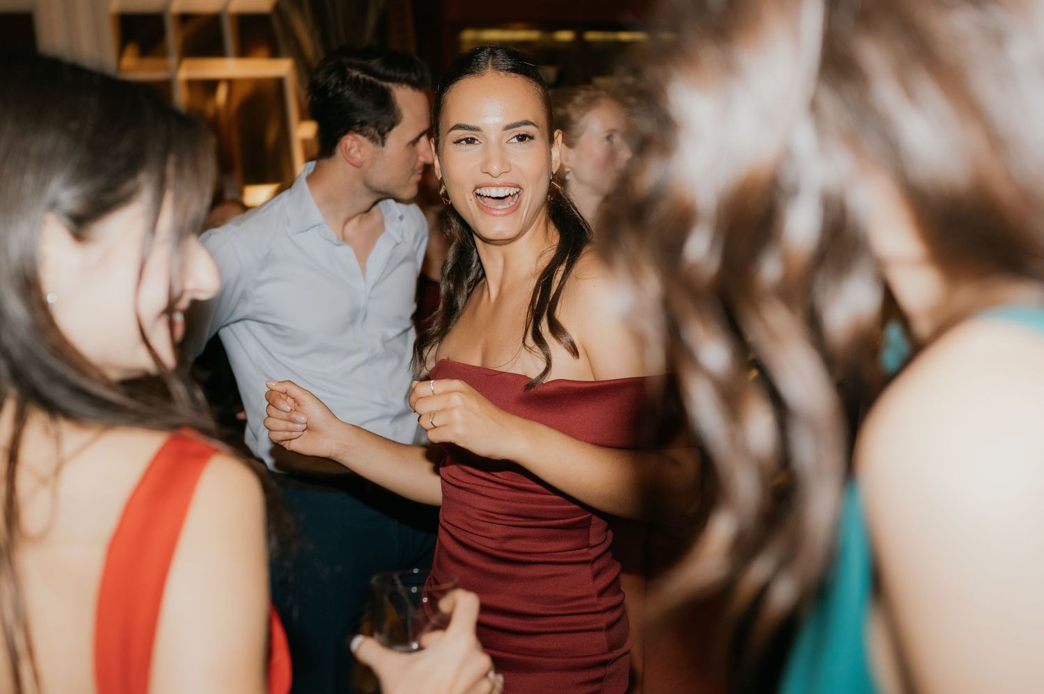Woman in red off-shoulder dress smiling and dancing at a party with guests in background.