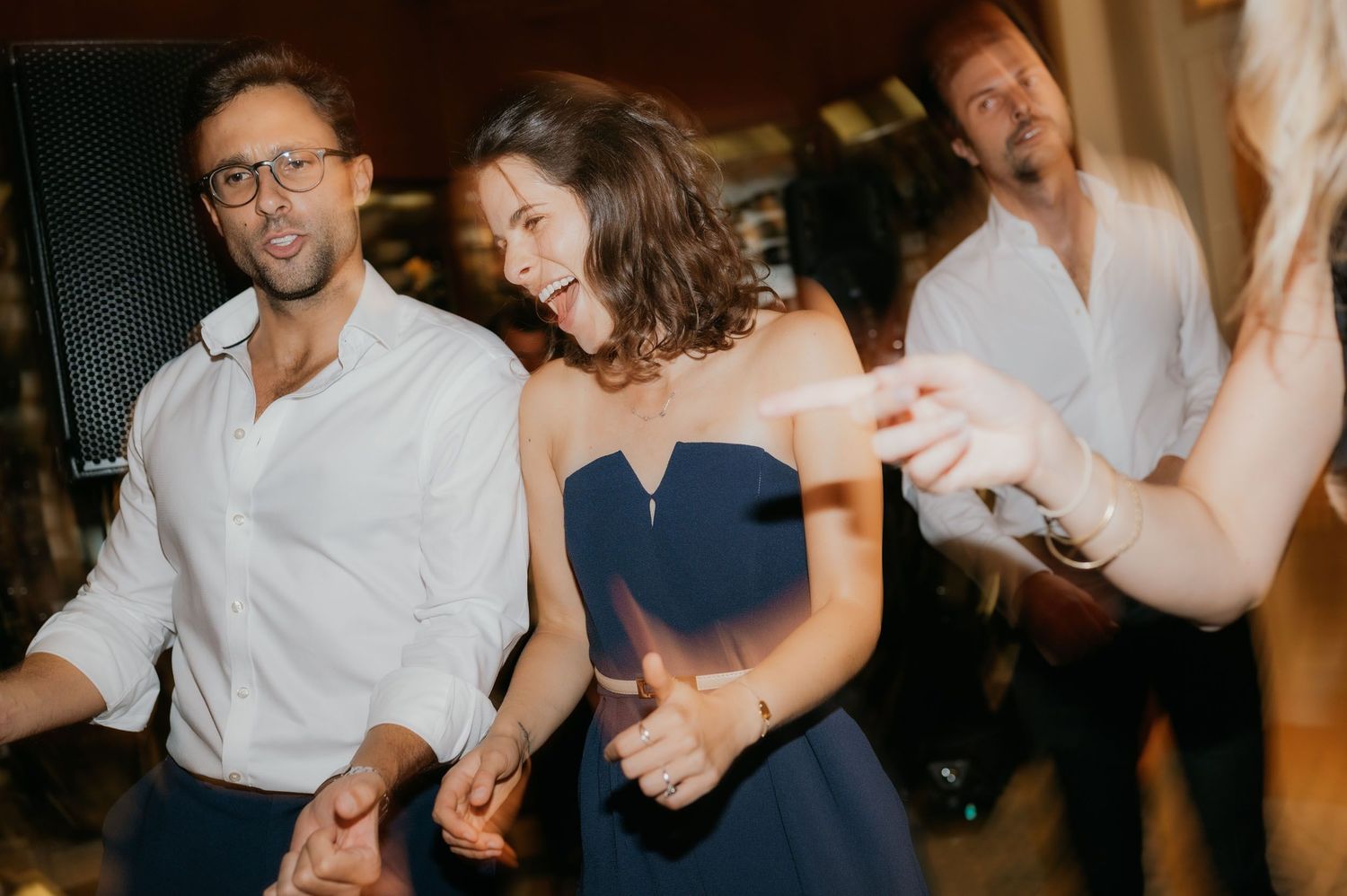 Guests dancing joyfully at a wedding reception, woman in blue dress laughing with man in white shirt.