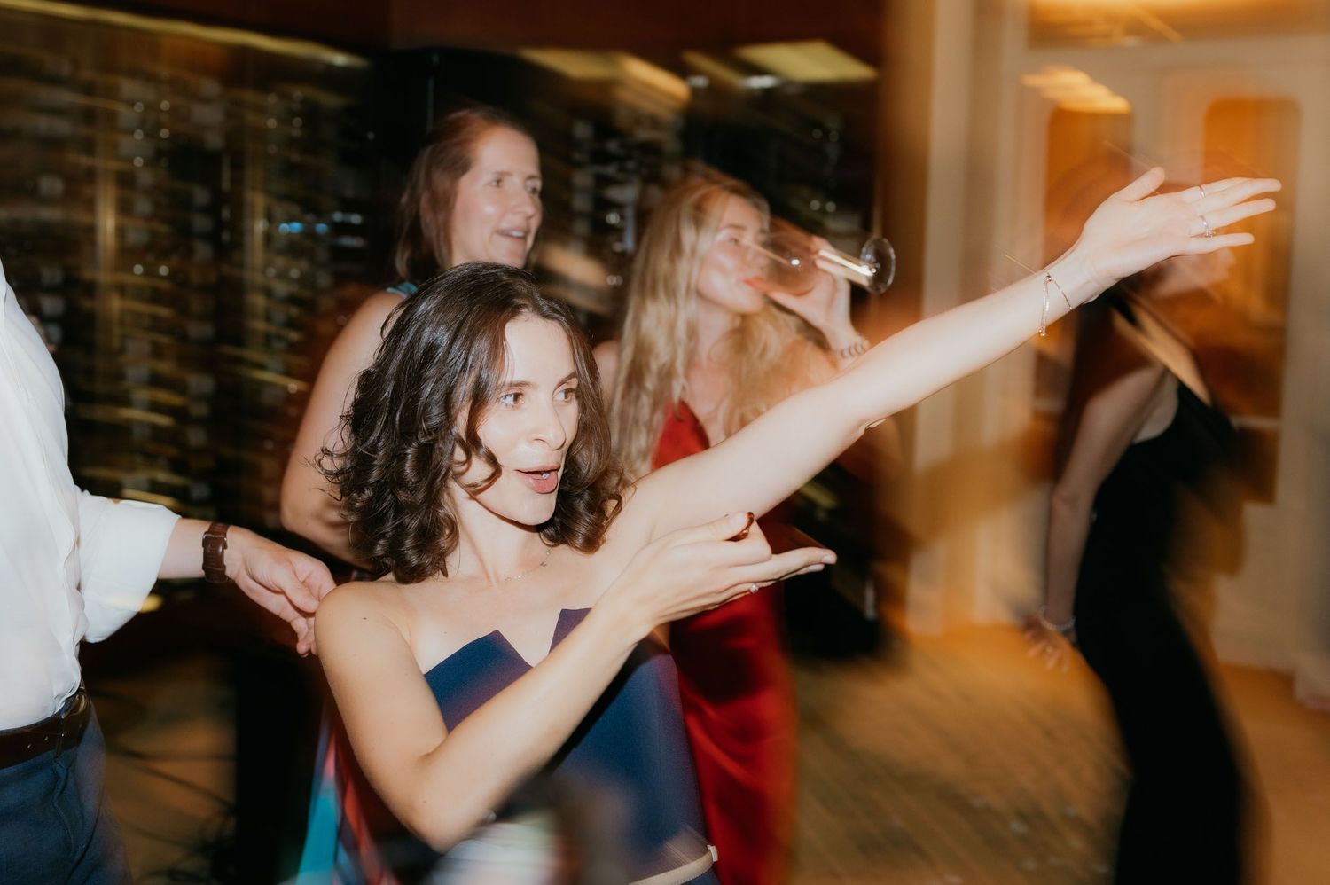 Women in formal dresses dancing energetically at an elegant evening party or wedding reception.