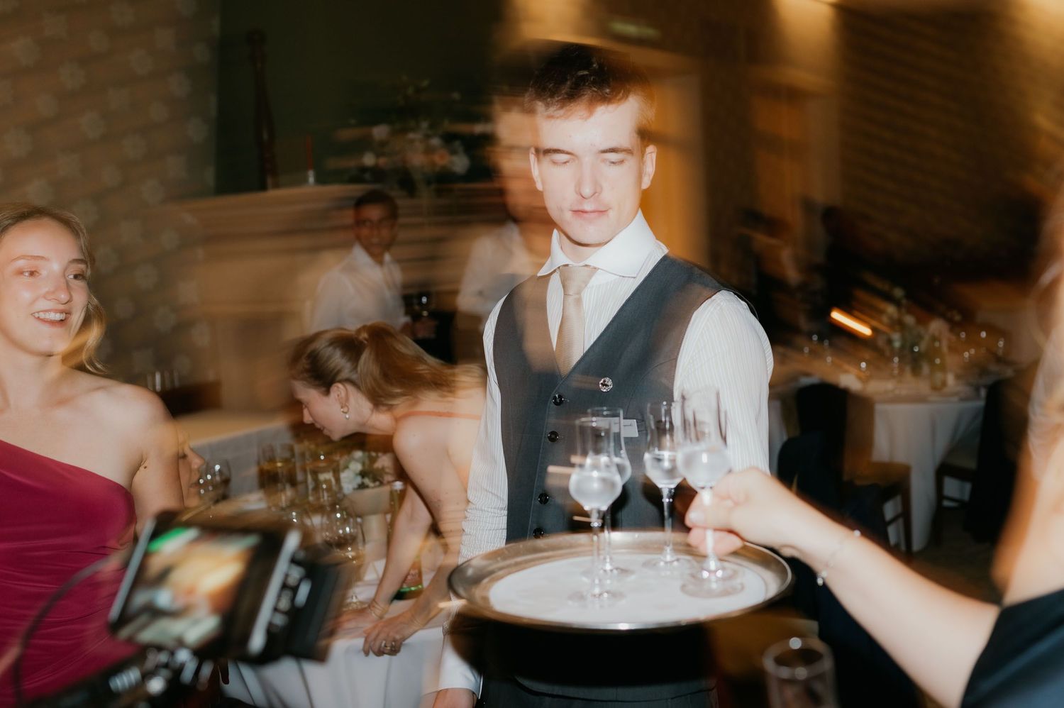 A waiter in a vest carries a tray of wine glasses at an elegant wedding reception.