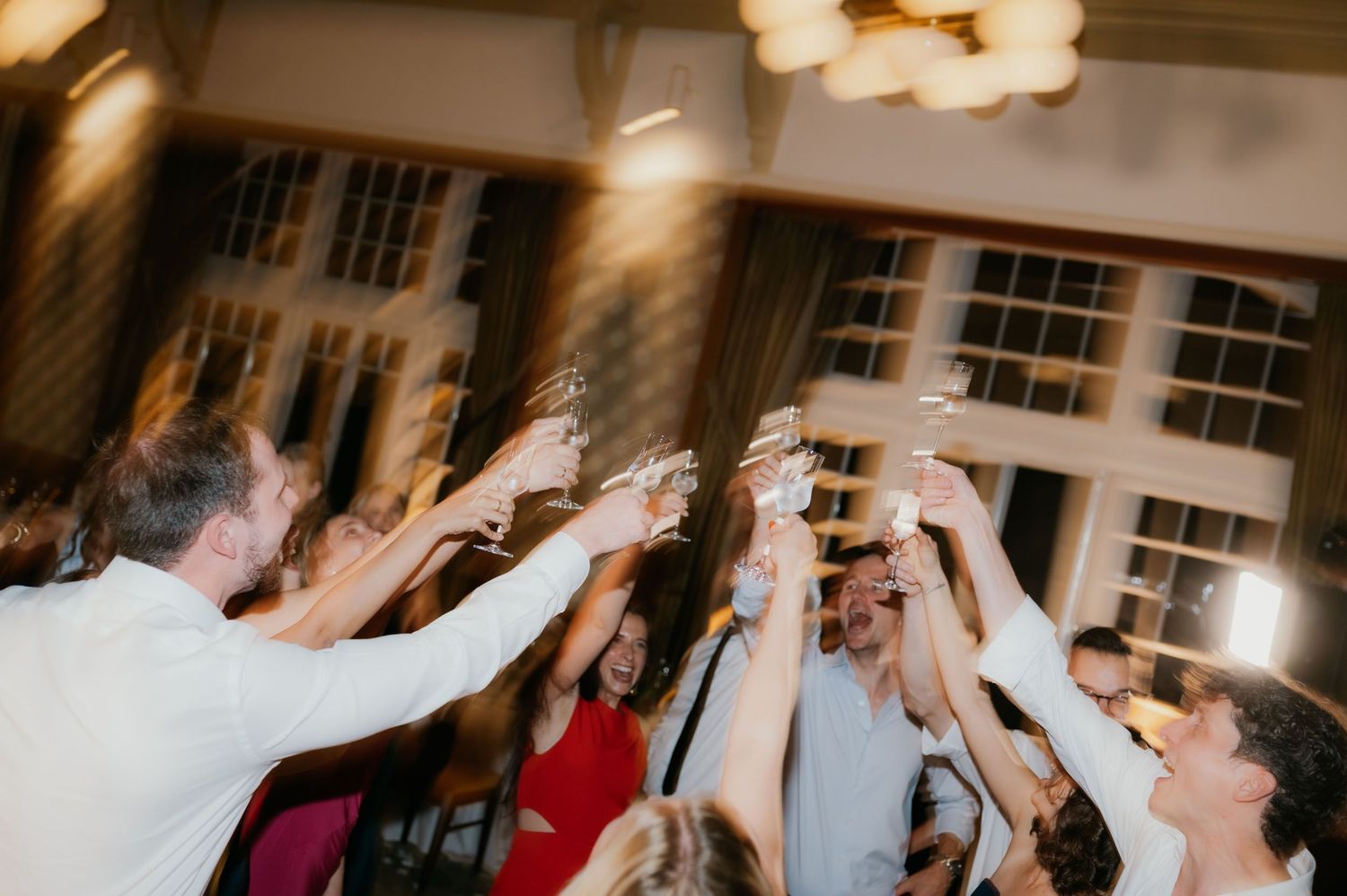 Wedding guests raising champagne glasses in a celebratory toast at an elegant indoor reception venue.