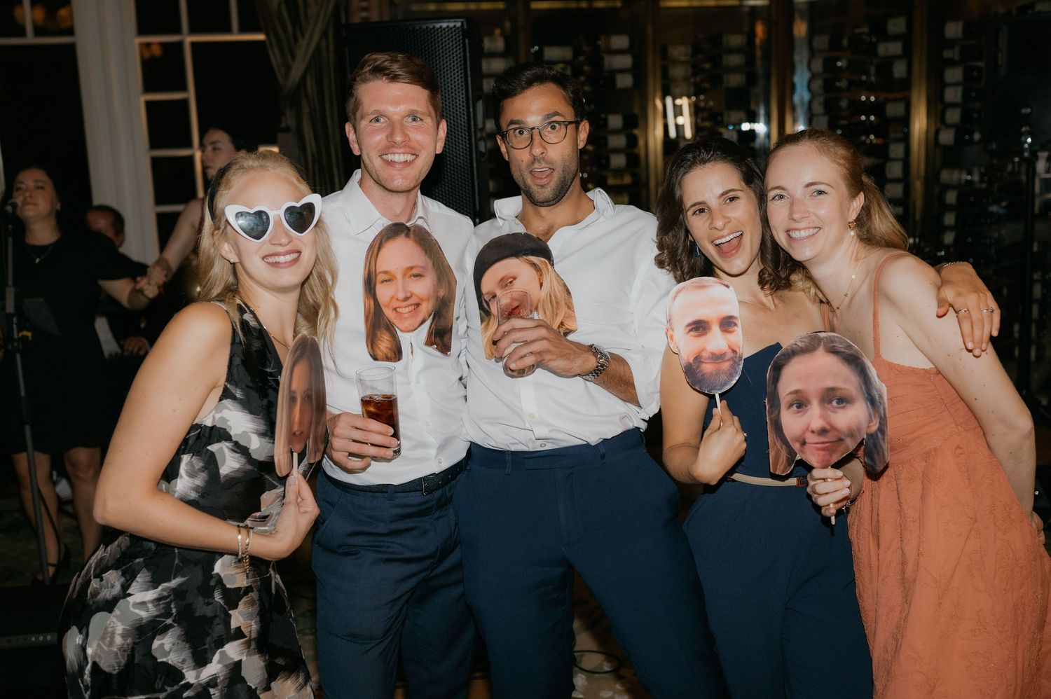 Group of friends posing with oversized face cutouts at a festive wedding reception party.