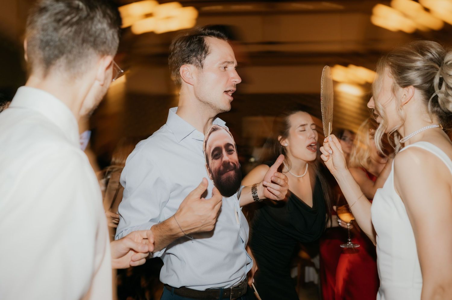 Wedding guests dancing and celebrating joyfully at a lively indoor wedding reception party.