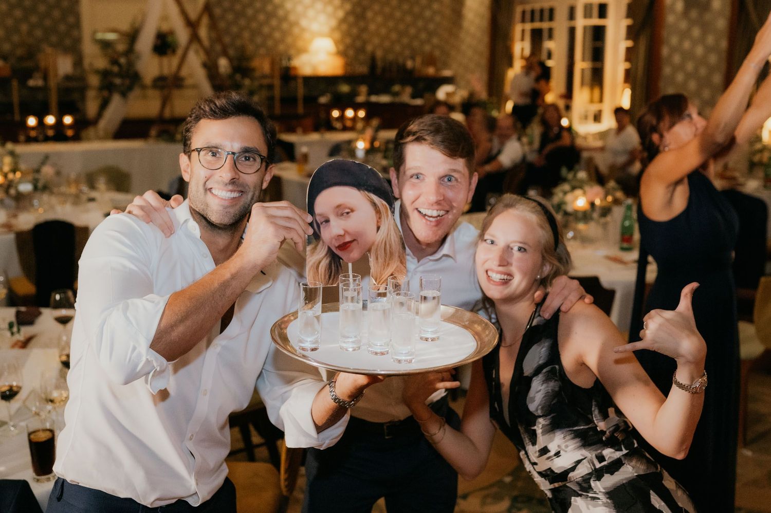 Four friends smile and pose with a tray of shot glasses at a festive wedding reception celebration.