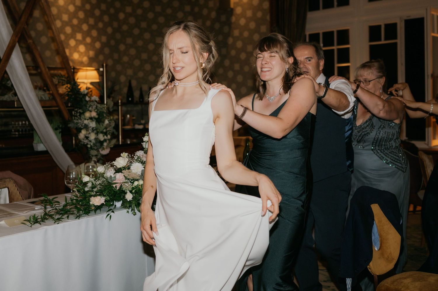 A bride in a white gown dances joyfully with guests at her wedding reception.