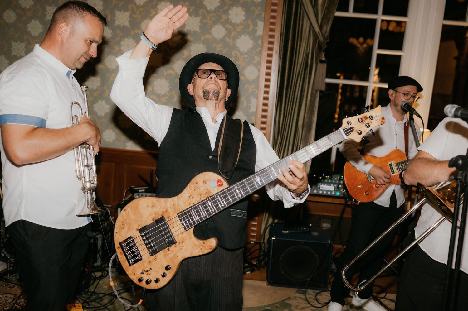 Live band performing at an event, featuring a bassist, trumpet player, and guitarist playing energetically indoors.