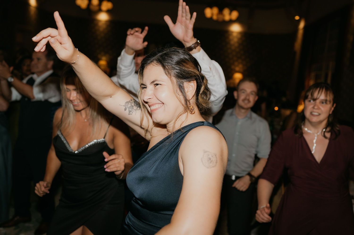 Woman in black dress dancing joyfully with hands raised at a wedding reception party.