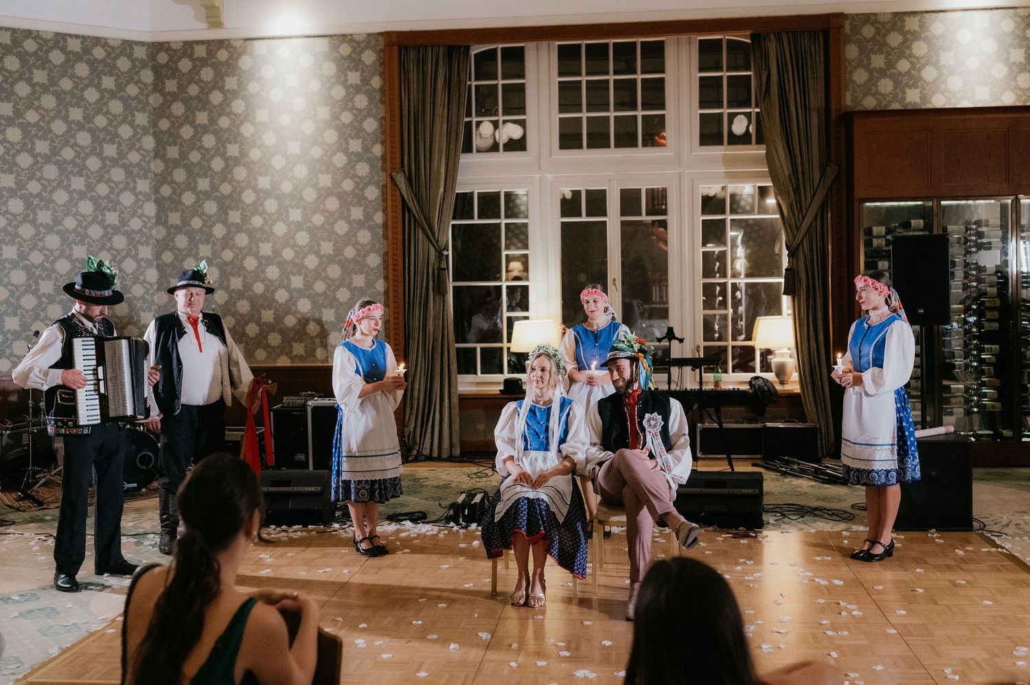 Folk dancers in traditional blue and white costumes perform on stage with accordion player at cultural event.