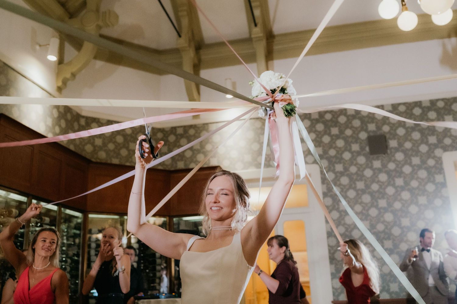 Bride smiling and holding a floral bouquet with colorful ribbons at a wedding reception.