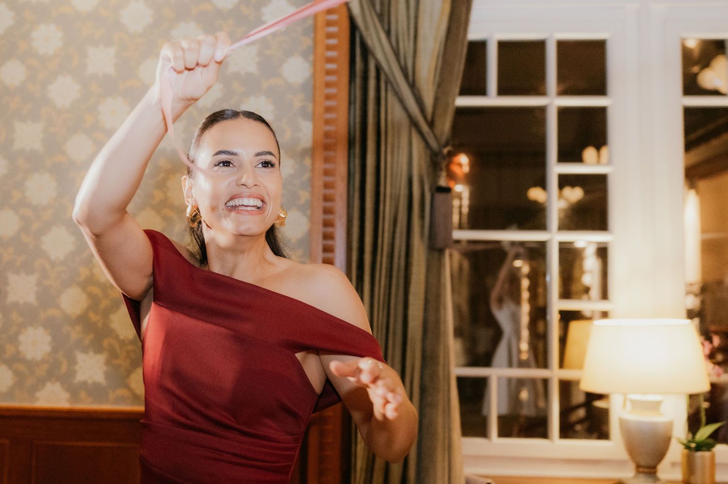 Woman in red dress pulling a ribbon at an elegant indoor wedding event.