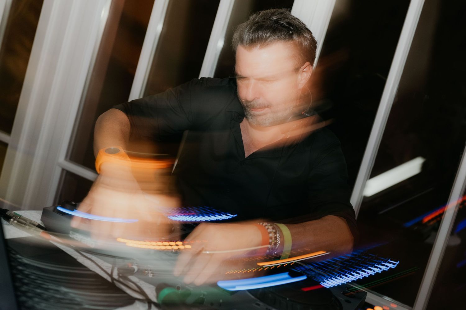 A DJ performing with motion blur effects, colorful lights illuminating turntables at a lively nightclub event.