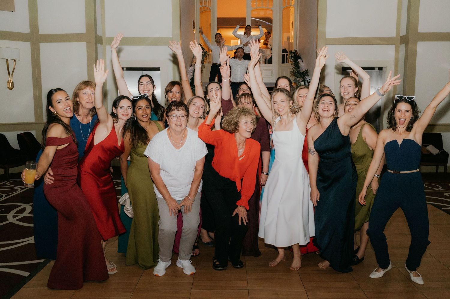 Group of women celebrating at a formal event, raising hands joyfully in an elegant venue.