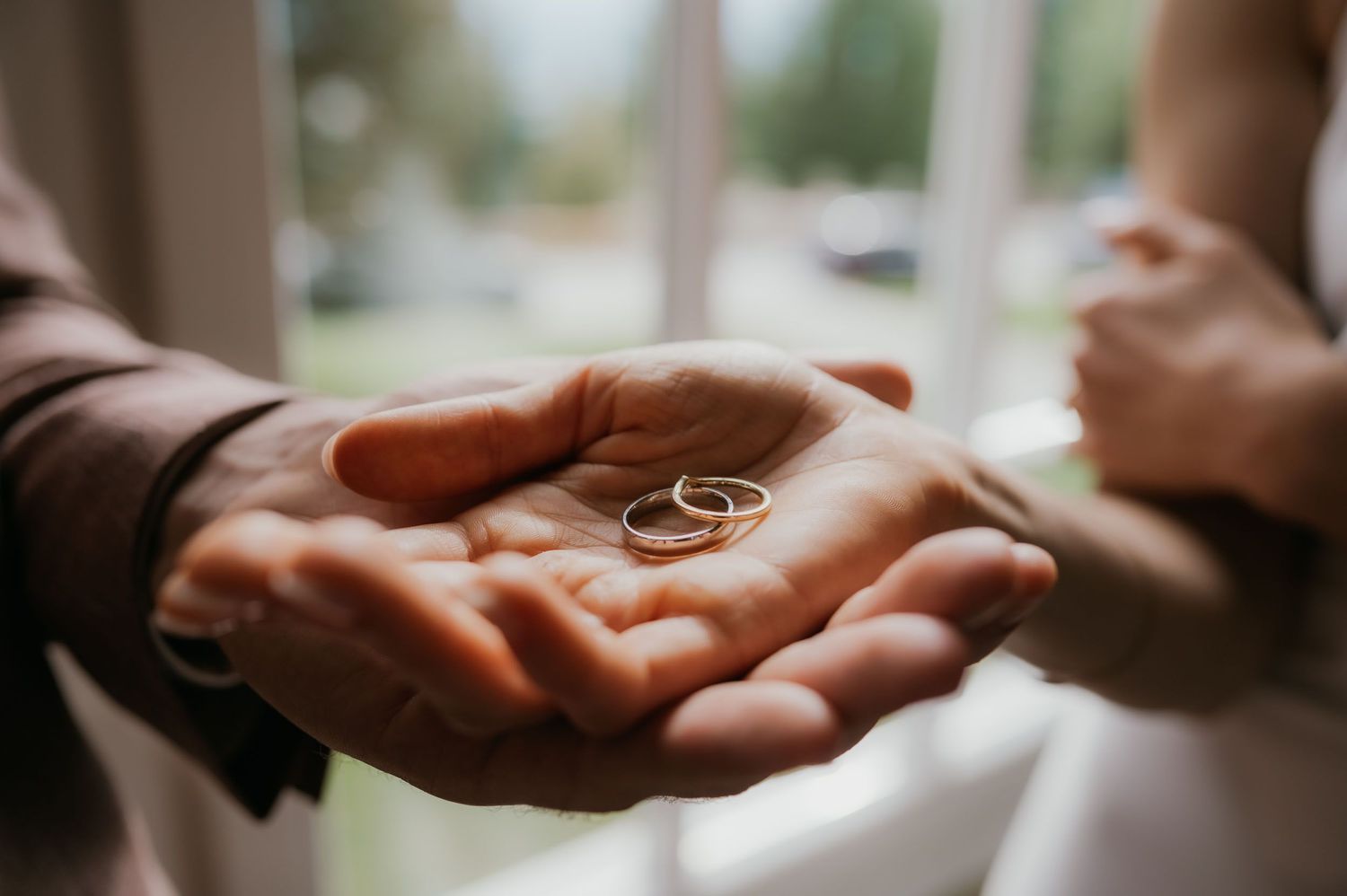 Two gold wedding rings resting on an outstretched hand during a wedding ceremony.