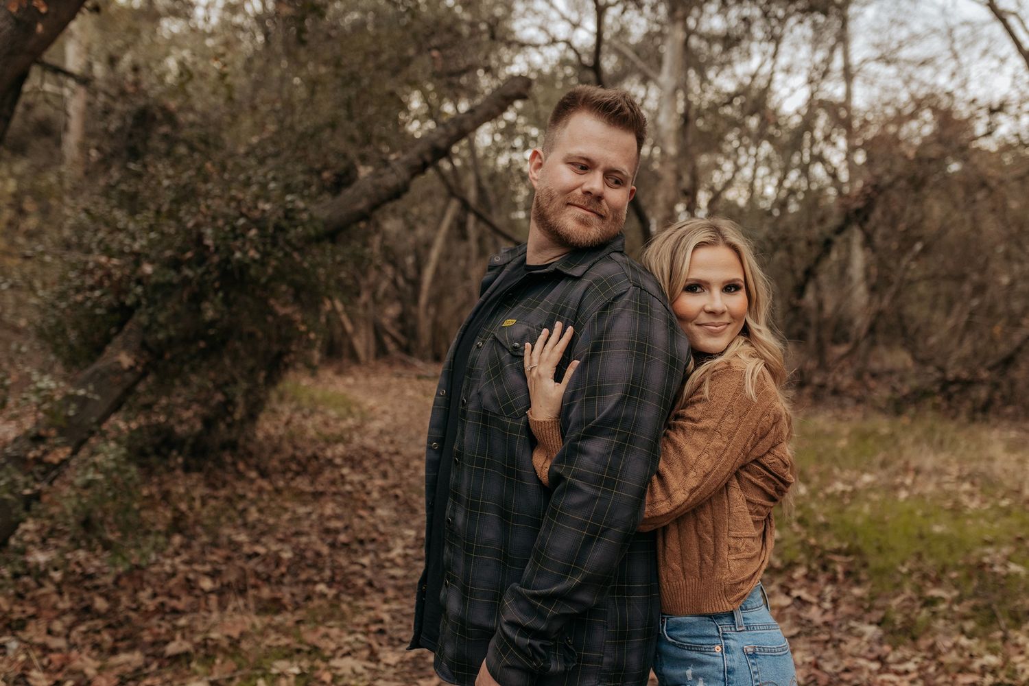 A couple shares intimate moments while walking through an autumn forest setting during a photo session in San Diego.