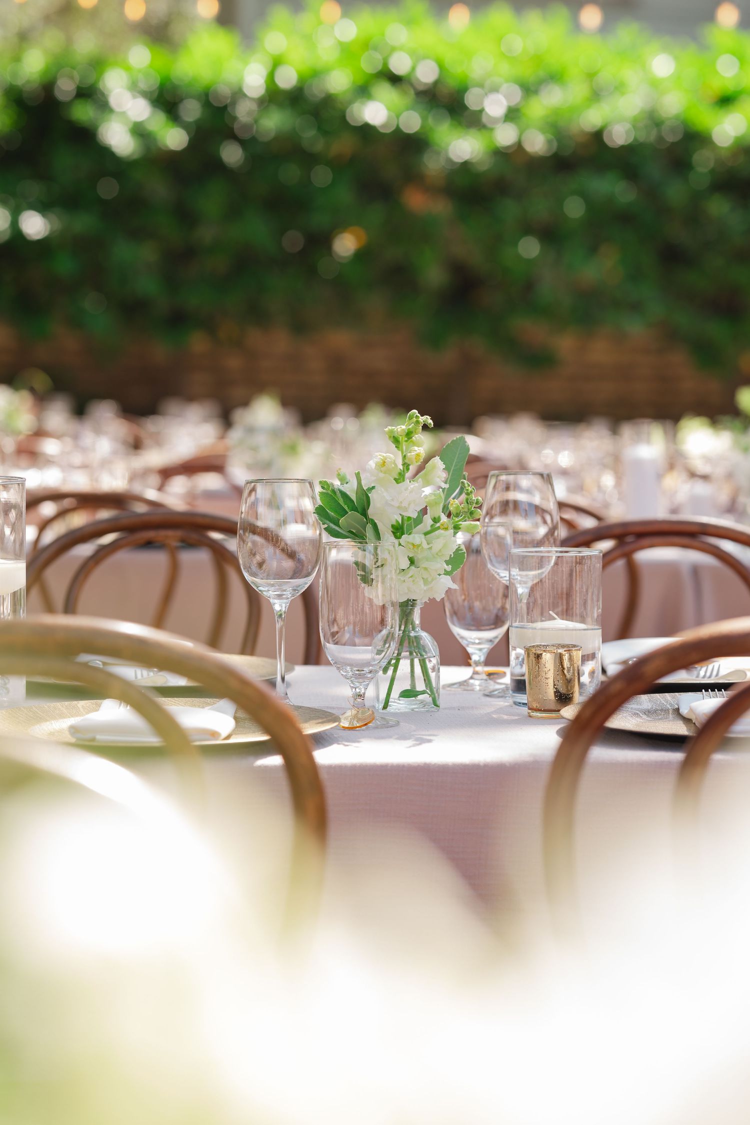 Long banquet tables set with white linens and wooden chairs create an elegant dining arrangement for a special event.