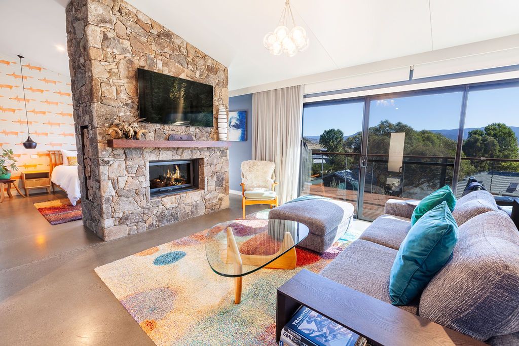 Modern mountain home interior features stone accent walls, panoramic windows, and contemporary furnishings with scenic views.