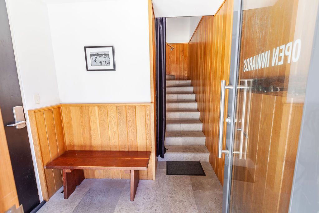 Wooden paneled hallway with multiple doors and a staircase leads to different rooms in a building interior.