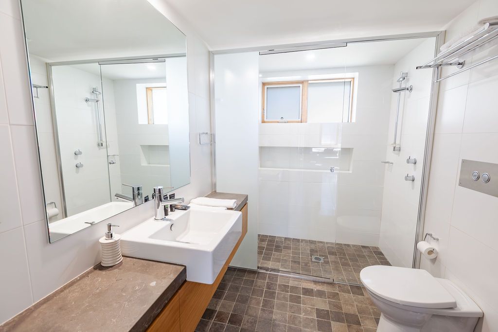 Contemporary white bathroom with tiled floor, wall-mounted sink, and natural light from window.