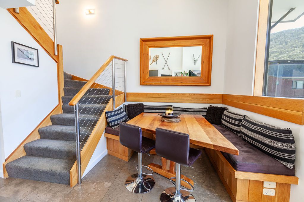 Modern wooden staircase with glass panels and metal railings leads upstairs in an open-concept home interior.