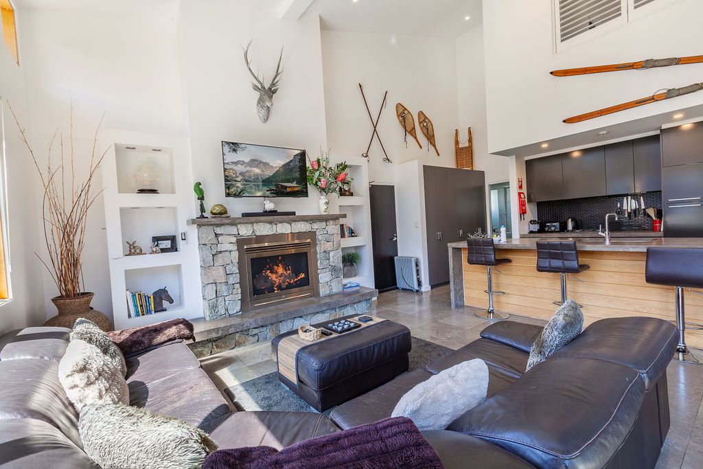 Contemporary living room features grey sectional sofa, high ceilings, and large windows with mountain views.