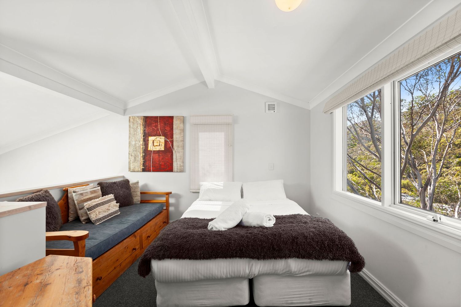 A bright modern loft bedroom with white walls, sloped ceiling, and large windows letting in natural light.