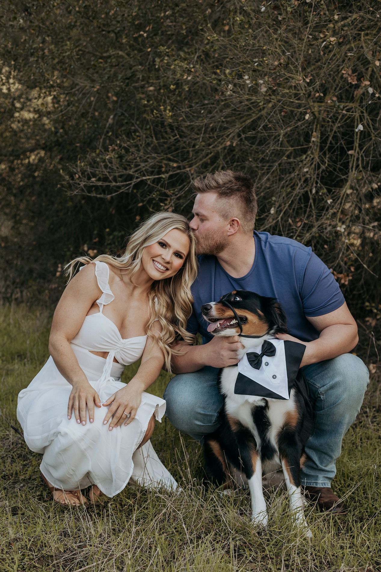 A couple sits in grass with their black and white border collie dog during an outdoor photo session in San Diego.