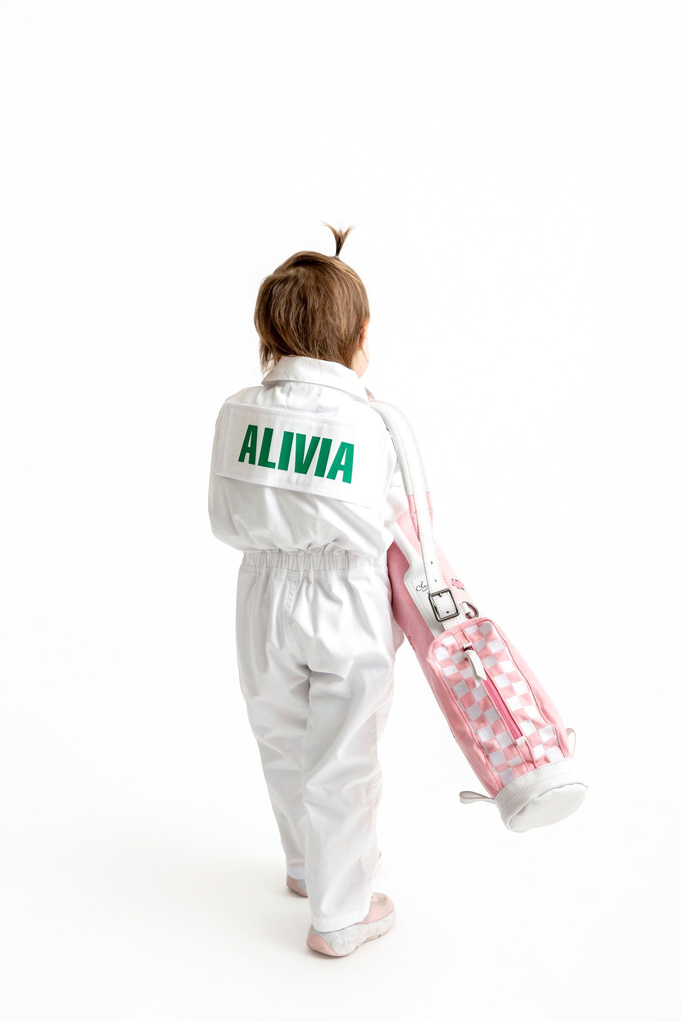 Small child wearing personalized white coveralls with name on back crawls away on white background.