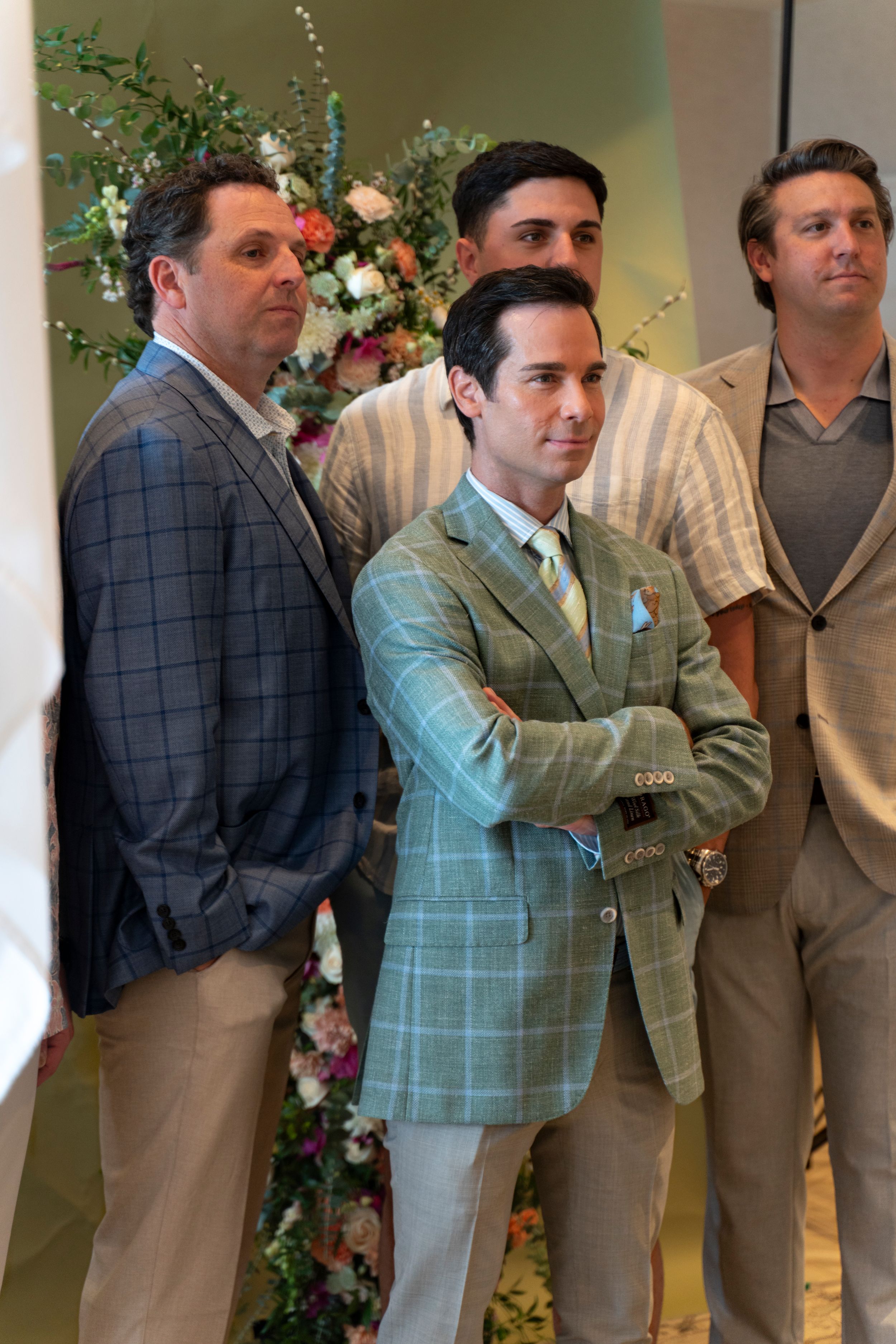 Row of men in formal attire standing against a wall decorated with floral arrangements. North Carolina Azalea Festival Spring Fashion Show