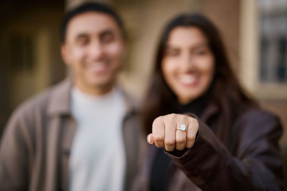 Happy couple showing off diamond engagement ring, smiling outdoors in a romantic proposal moment.