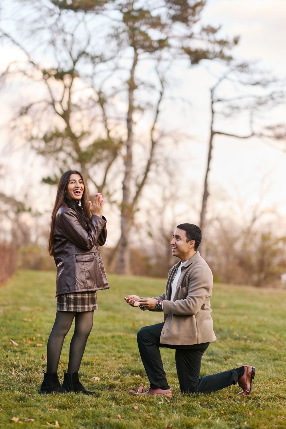 Man proposing on one knee to surprised woman in autumn park, romantic outdoor marriage proposal scene.
