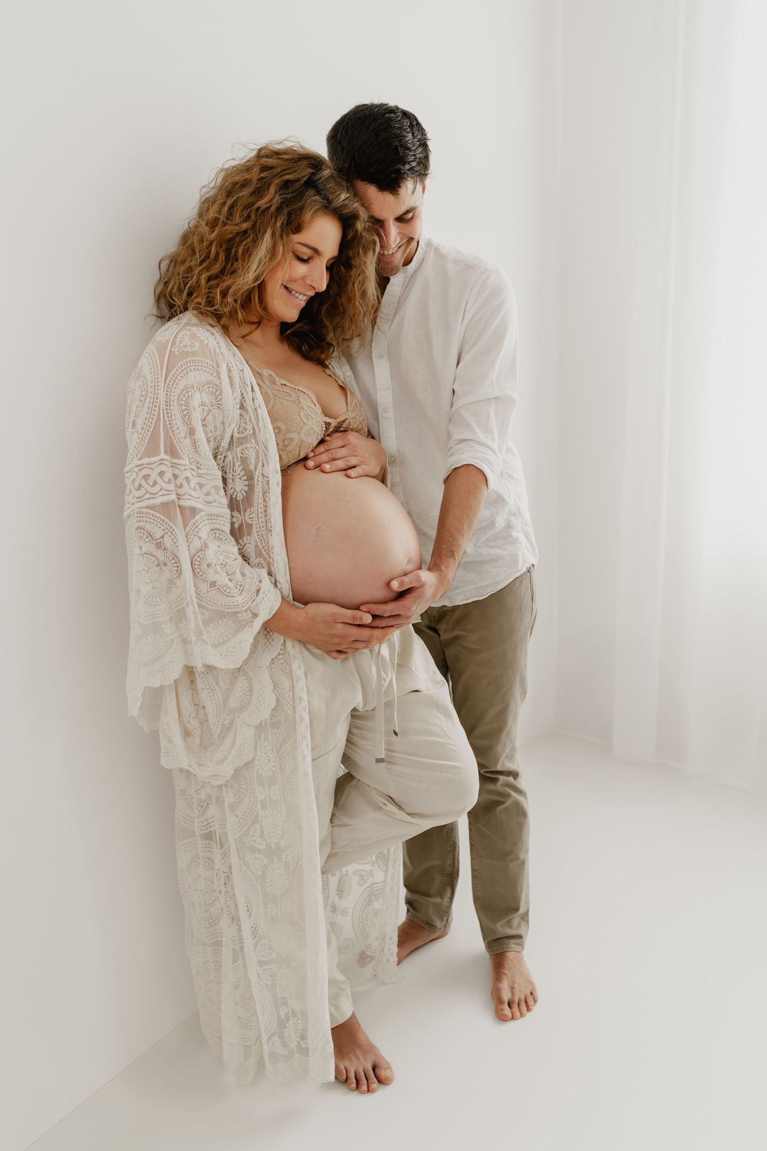 Paar beim Babybauchfotoshooting im Fotostudio Wien, Hände des Paares halten sanft den Babybauch