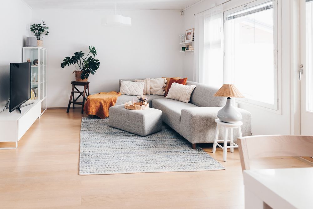 Modern minimalist living room interior with white walls, wooden floors, and natural light streaming through windows.